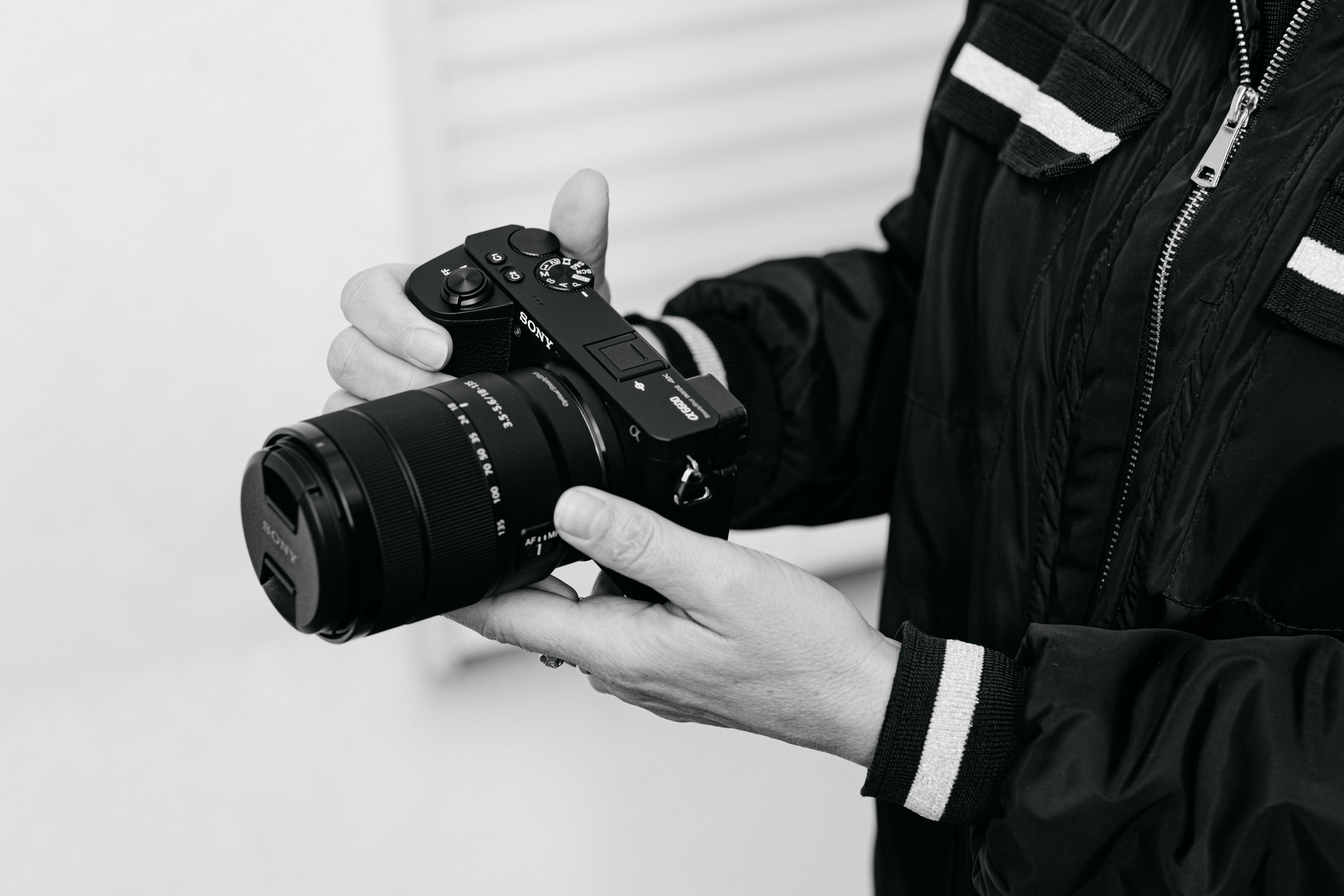 Grayscale Photo of a Person's Hands Holding a Sony Camera